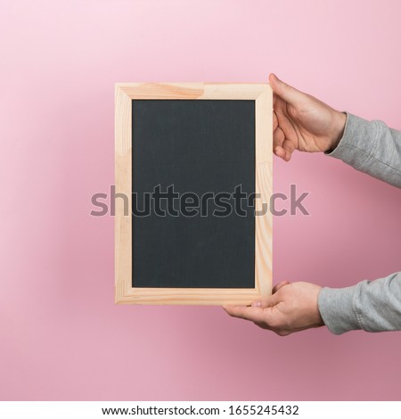 Men's hands hold a black board, an empty blank, a frame, on a pink background. Copy space.