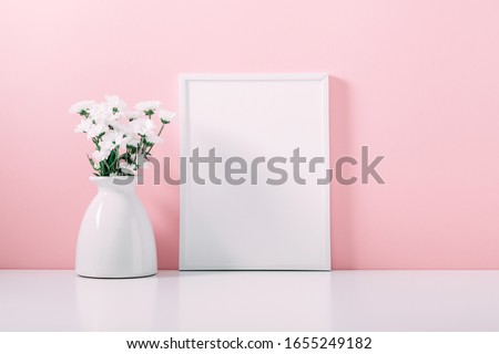 Front view blank mock up of photo frame on pink background. 
Home interior floral decor. Beautiful flowers in  vase on pink wall background.