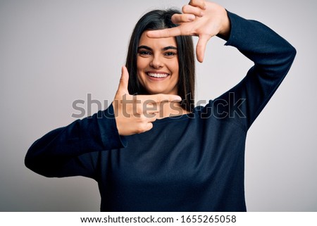 Young beautiful brunette woman wearing casual sweater standing over white background smiling making frame with hands and fingers with happy face. Creativity and photography concept.