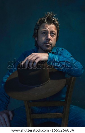 Man in denim shirt with cowboy in hand on chair.