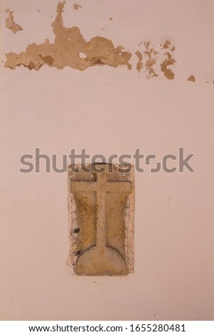 Old stone cross with letters INRI (Iesus Nazarenus Rex Iudaeorum - Jesus from Nazarath, King of the Jews) in the light orange wall of a building. Estoi, Portugal.