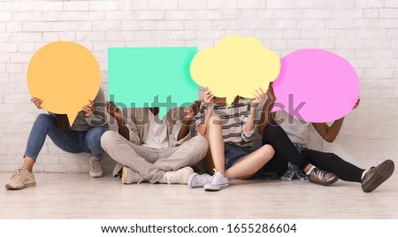 Group of multiracial teen friends covering faces with colorful speech bubbles over white brick wall, student community concept Royalty-Free Stock Photo #1655286604