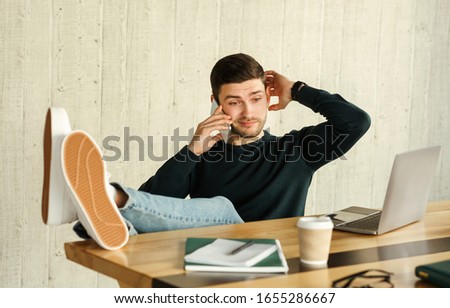 Irresponsible Worker. Confused Freelancer Talking On Phone Delaying Deadline And Procrastinating Sitting At Workplace Indoor. Selective Focus Royalty-Free Stock Photo #1655286667