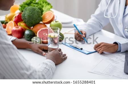 Detox concept. Afro woman patient of nutritionist drinking lemon water while doctor taking notes, close up Royalty-Free Stock Photo #1655288401