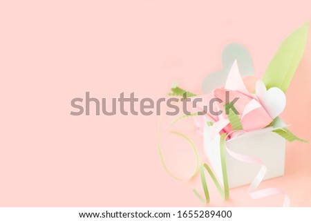 Banner with composition of pink origami paper tulip with green decorations in white box with hearts on pink background. Copy space. Handmade art project. DIY concept