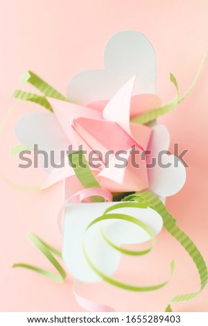 Closeup composition of pink origami paper tulip with green decorations in white box with hearts on pink background. Copy space. Handmade art project. DIY concept