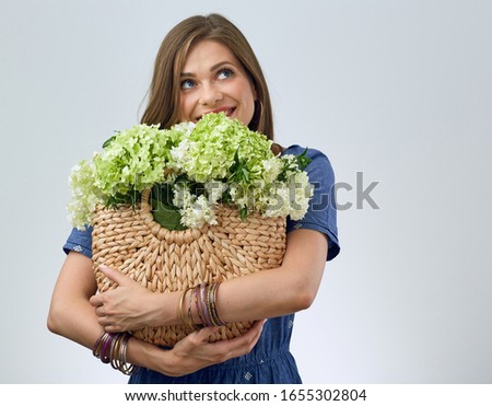 Isolated portrait of smiling woman holding flowers in straw hand bag and looking up.