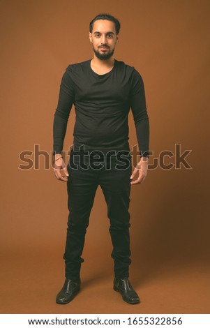 Young bearded Indian man against brown background
