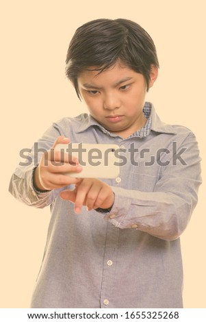 Studio shot of cute Japanese boy taking picture with mobile phone