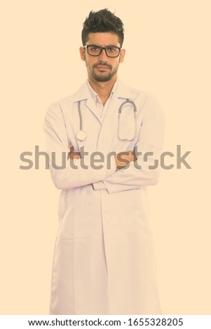 Studio shot of young Persian man doctor standing with arms crossed