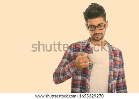 Studio shot of young Persian man holding and looking at coffee cup