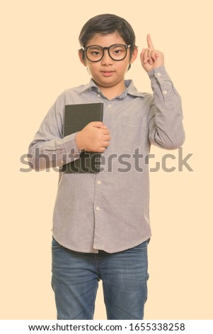 Studio shot of cute Japanese boy holding book and pointing finger up