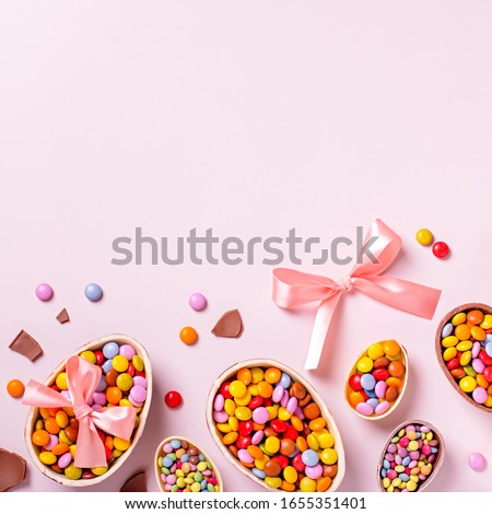 Chocolate Easter border with chocolate eggs and colorful candy sweets on pastel pink, copy space. Traditional Easter treats flat lay, holiday background