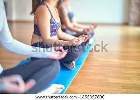 Young beautiful group of sportswomen practicing yoga. Doing lotus pose at gym