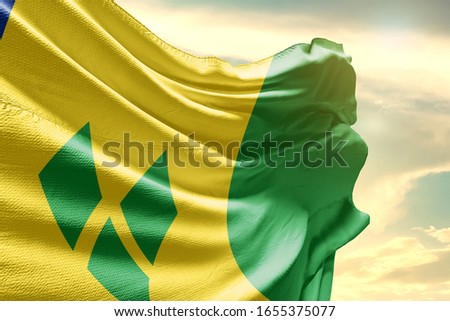 Saint Vincent and the Grenadines national flag cloth fabric waving on the sky with beautiful sun light.