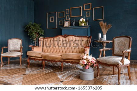 Modern dark interior with a fireplace, flowers, a cozy brown sofa with carved legs and two elegant armchairs. The stylization of the Baroque, classical design, historic interior. Royalty-Free Stock Photo #1655376205