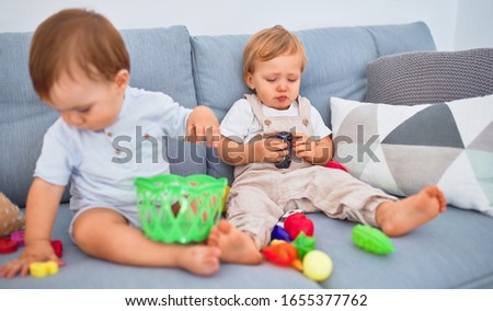Beautiful toddlers, one of them crying, sitting on the sofa playing with toys at home