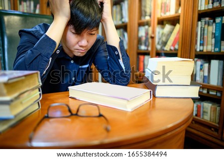 Smart Asian man university student feeling stressed and anxious while reading book by vintage bookshelf in college library for education subject and research. Scholarship for education opportunity. Royalty-Free Stock Photo #1655384494