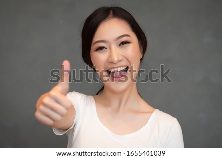 successful girl pointing thumb up; portrait of cheerful smiling woman pointing up approving, yes, ok, good, thumb up gesture; Chinese or east asian woman young adult model