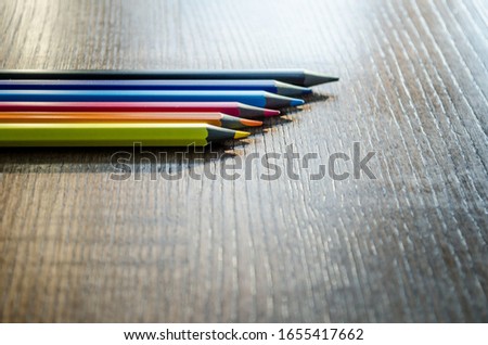 Six colored pencils lie on a dark wooden table in the sunlight