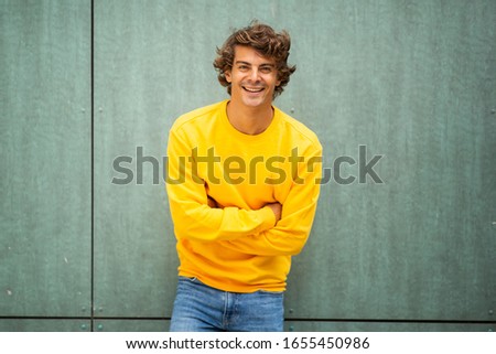 Portrait male fashion model in yellow sweater smiling by green background