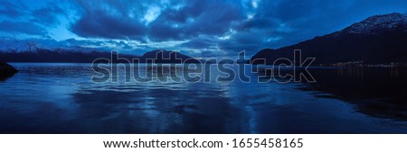 Panoramic view of Hardanger fjord at twilight. Beautiful Norwegian landscape with clouds and mountains reflected in the water at blue hour. Ålvik village, Hordaland, Norway.