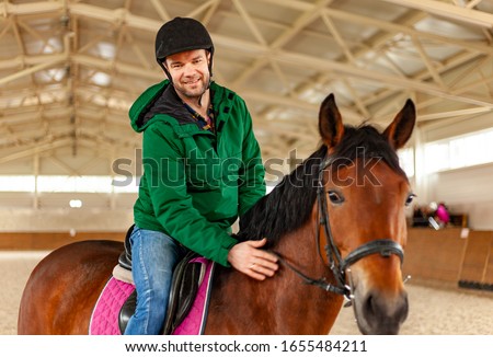 man jockey sitting on horse, horseback training on manege, lesson for  jockey in equestrian school or club, pet animal  Royalty-Free Stock Photo #1655484211