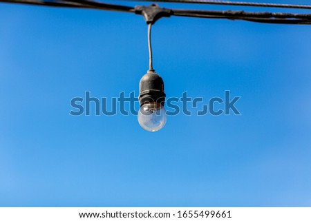Light bulbs with a beautiful blue sky background - summer in nature concept. Electric garland for lighting with white light bulbs against the background of a blue clear sky
