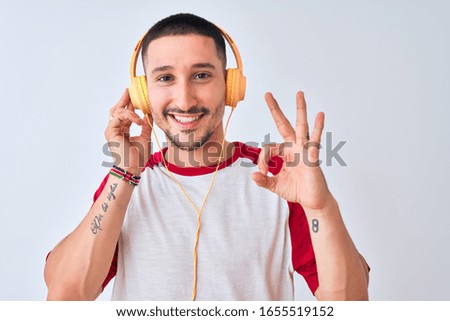 Young handsome man wearing headphones over isolated background doing ok sign with fingers, excellent symbol