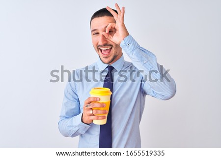 Young business man holding take away coffee over isolated background with happy face smiling doing ok sign with hand on eye looking through fingers