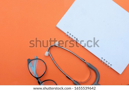 copy space medical Stethoscope and glasses notebook on orange background. in doctors desk