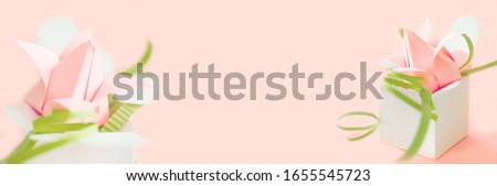 Banner with composition of pink origami paper tulip with green decorations  in white box with hearts on pink background. Copy space. Handmade art project. DIY concept