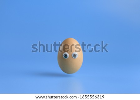 One brown egg with eyes on a blue background. Minimal Happy Easter concept decoration. Copy space for text mockup. Close up photography.