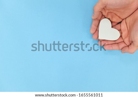 Hands holding a white heart in blue background with copy space. Kindness, charity, pure love and compassion concept. Royalty-Free Stock Photo #1655561011