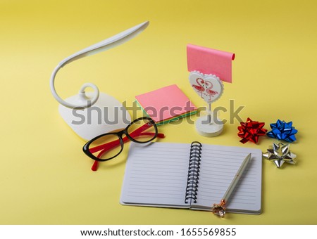 Notepad, table lamp, glasses and pencil on yellow background. Space for text. Top view, space for text 