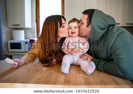 Intimate family life, a couple, husband and wife with a newborn baby girl in the home kitchen - The man and the woman kissing the child together on the cheeks