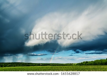 Nature background. Rainclouds and rain over the field with rainbow Royalty-Free Stock Photo #1655628817
