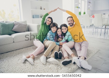 Portrait of nice attractive careful cheerful adorable ideal family three pre-teen kids mom dad sitting on carpet floor showing making roof good change at cozy comfort light white interior style house Royalty-Free Stock Photo #1655650342