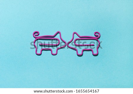 top view of two pink piggy paper clips in front of each other touching with noses on blue background