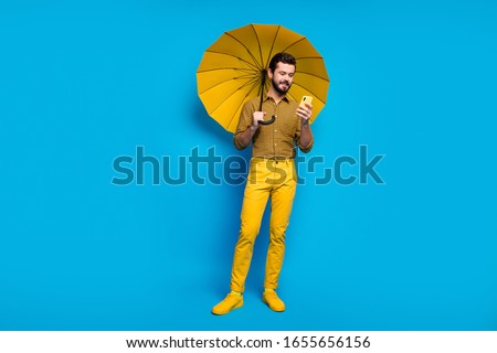 Full size photo of positive bearded student man use smartphone read social media news hold shine parasol shield wear style stylish trendy plaid trousers shoes isolated over blue color background