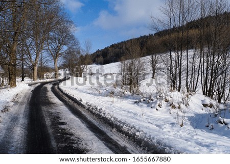 Winter rural landscape. A snow-covered road with melting snow. The beginning of spring on rural roads. Photo with space for text.