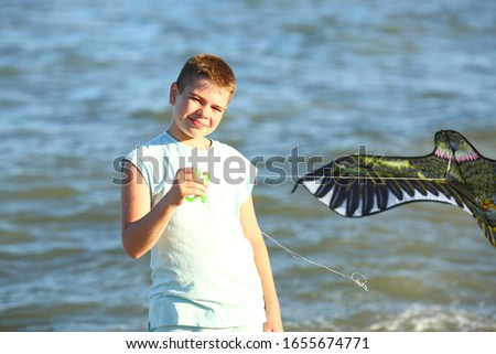 
handsome teenager boy launches kite on the sea in blue sky, close up