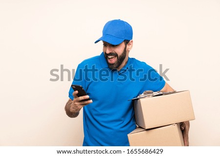 Delivery man with beard over isolated background with phone in victory position