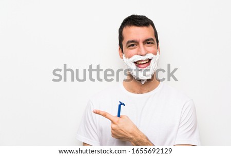 Man shaving his beard over isolated white background pointing to the side to present a product