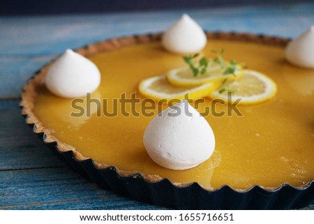 Lemon pie (tart) with meringue and butter cookie crust. Blue wooden table, lemon slices on top
