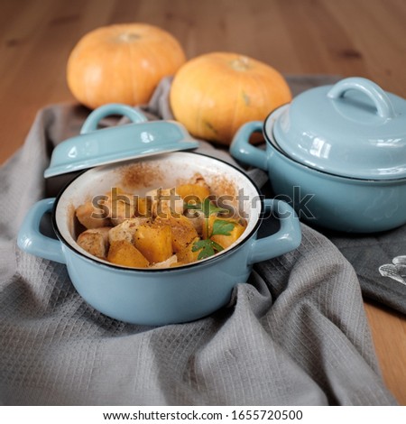 Roast pumpkin and chicken with spices in a blue pan on a wooden table, top view. Thanksgiving concept