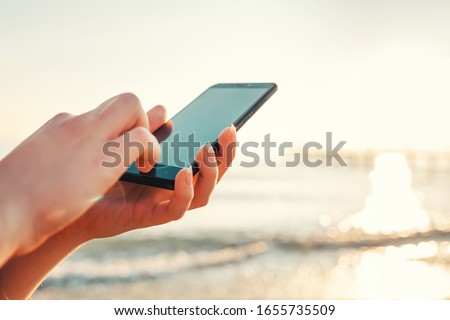 The concept of smartphones and the Internet. Female hands hold a smartphone and press something in it. In the background the sea. Copy space