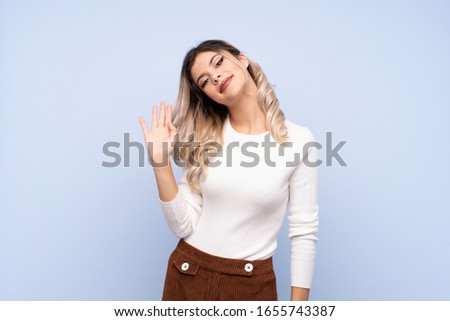 Young teenager girl over isolated blue background saluting with hand with happy expression