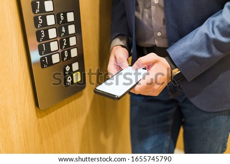 Unrecognizable businessman using mobile phone in elevator.