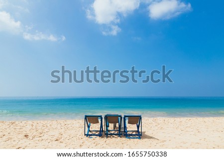 Three beach seats on a sandy ocean beach at beautiful vacation day under blue sky close to turquoise water on tropical resort.